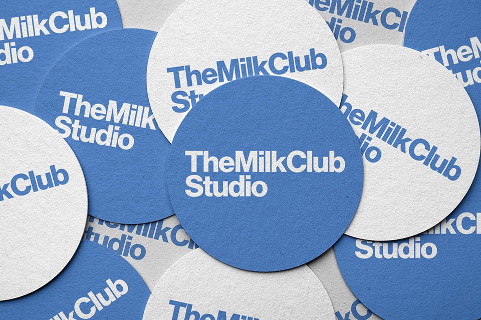 Blue and white circular stickers with the text 'The Milk Club Studio' printed on them, scattered randomly.