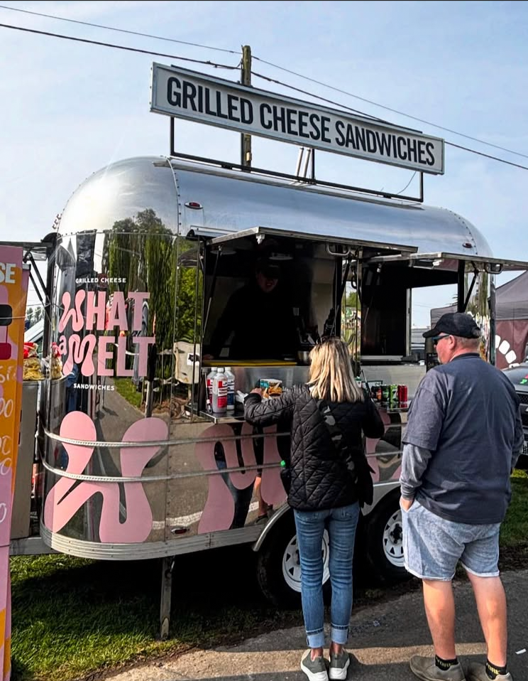 A food truck offering grilled cheese sandwiches at an outdoor event, with two customers ordering at the counter.