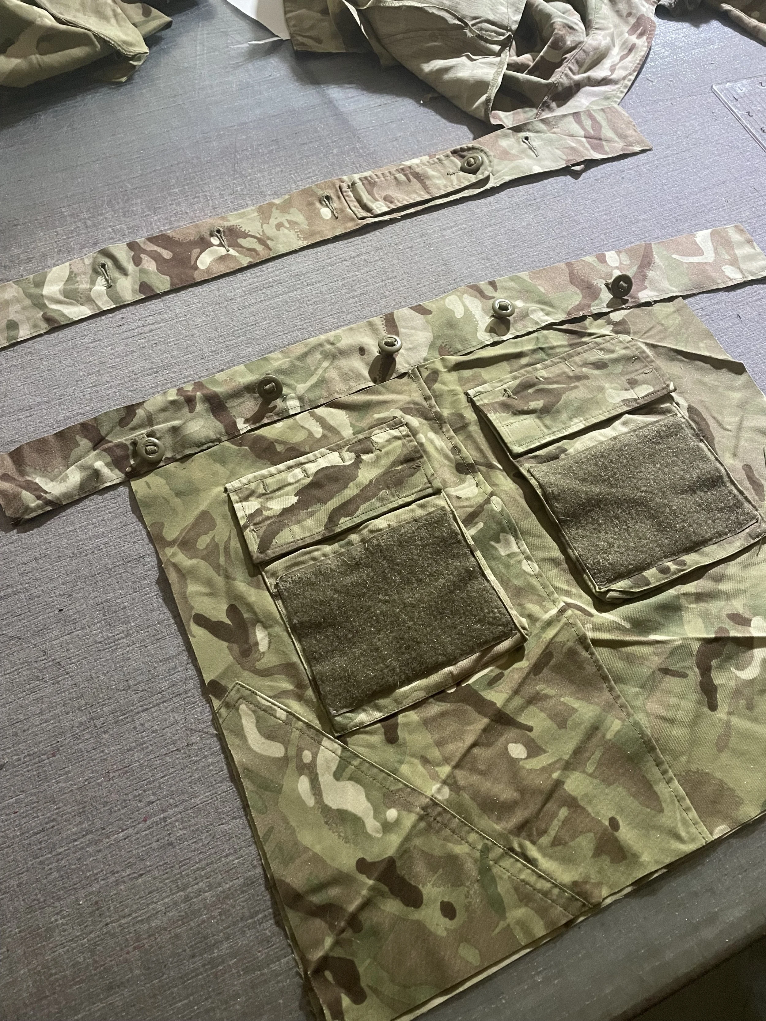 Camouflage military uniform with straps and pockets laid out on a table.