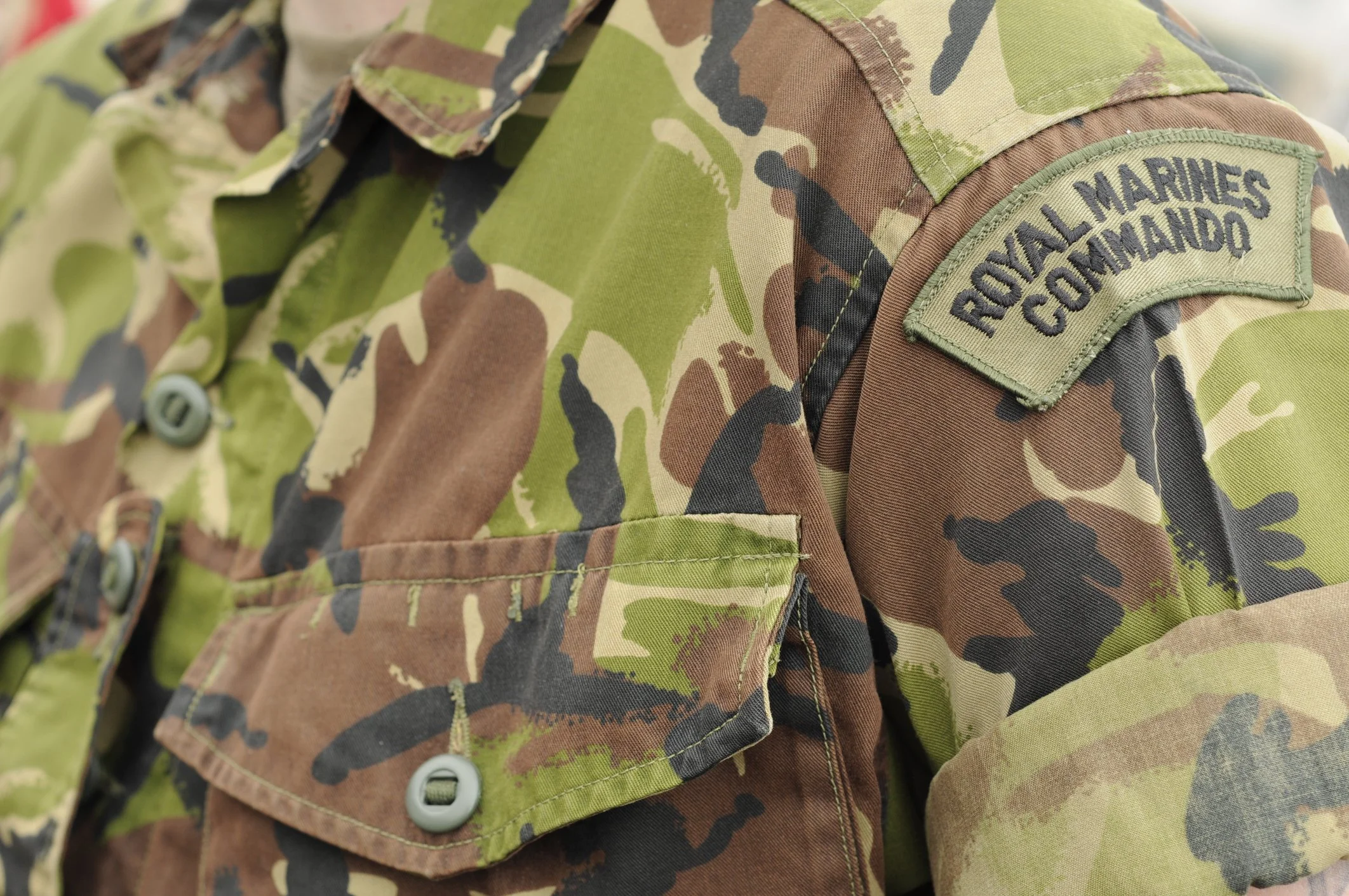 Close-up of a camouflage military jacket featuring a shoulder patch reading "Royal Marines Commando," illustrating the classic DPM (Disruptive Pattern Material) camouflage pattern used by the British Armed Forces.