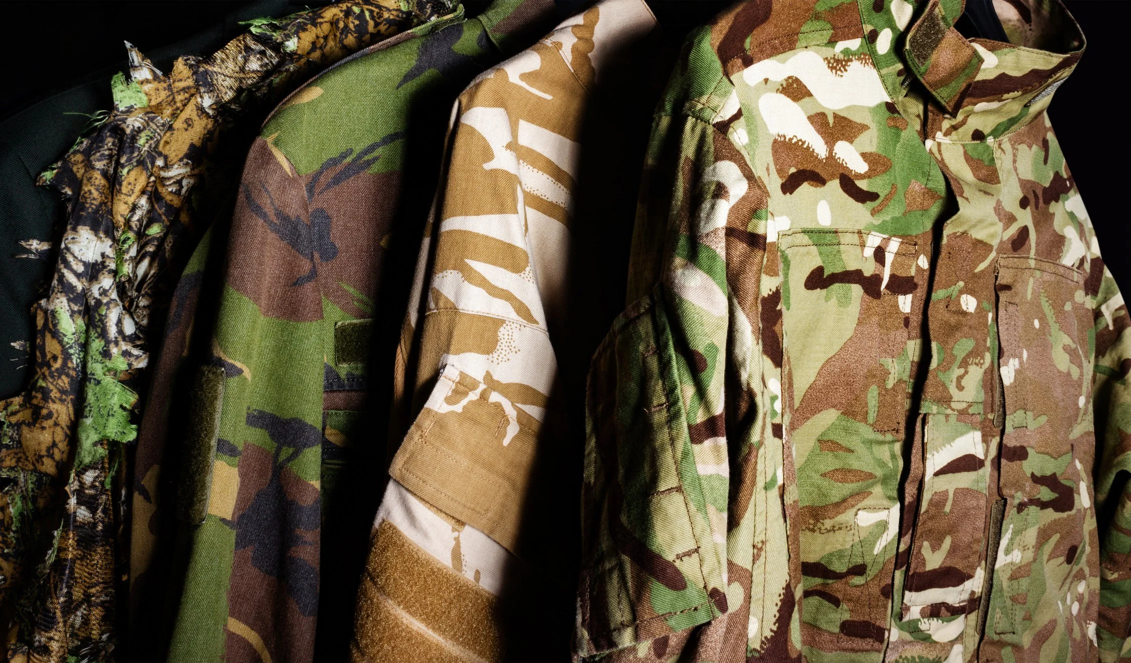 Multiple camouflage military shirts hanging on a rack, in various patterns and colors.