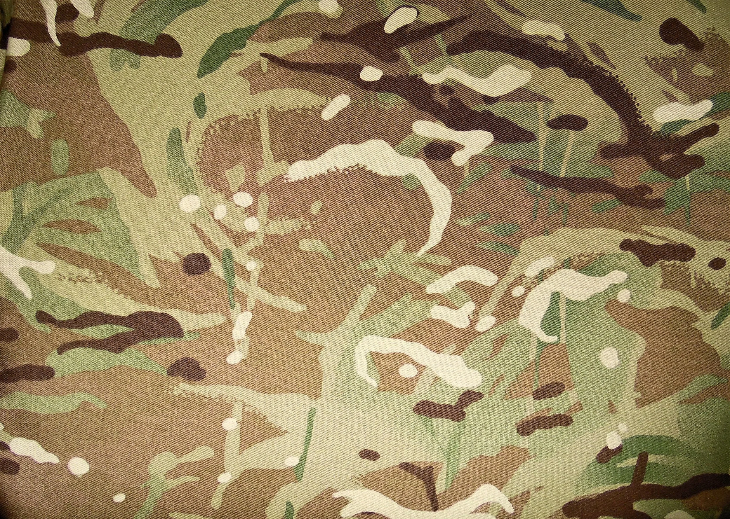 Close-up of British Multi-Terrain Pattern (MTP) camouflage fabric, showing the layered tan, green, brown, and cream colour palette developed to provide effective concealment across a wide range of environments.