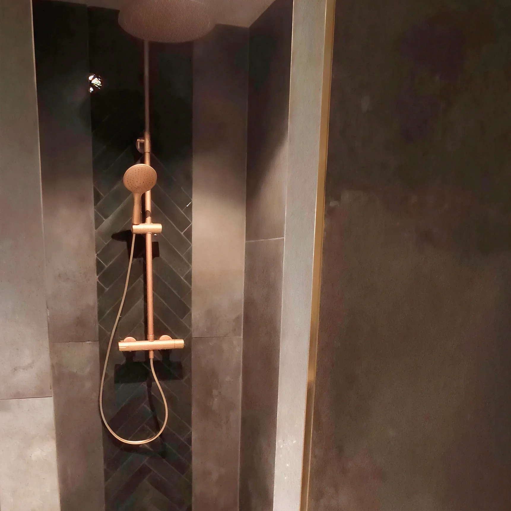 Douchette de salle de bain murale en acier inoxydable avec un raccordement au plafond, dans une cabine de douche moderne avec des carreaux gris.