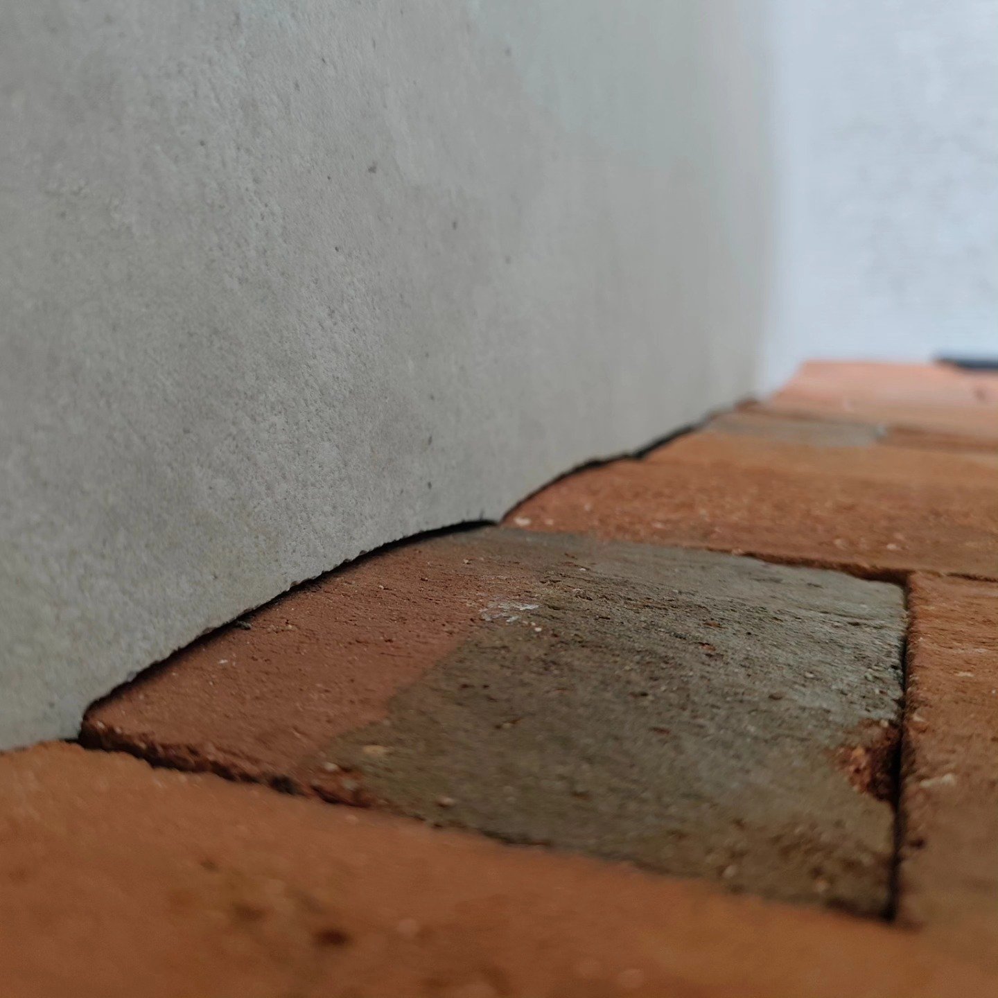 Gros plan d'une jonction entre un mur en plâtre et un sol en briques.