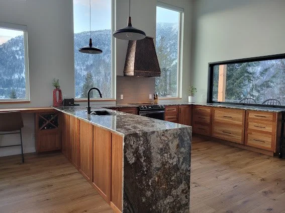 A bright kitchen with wood cabinets, grey marble counters and views of snowy mountains