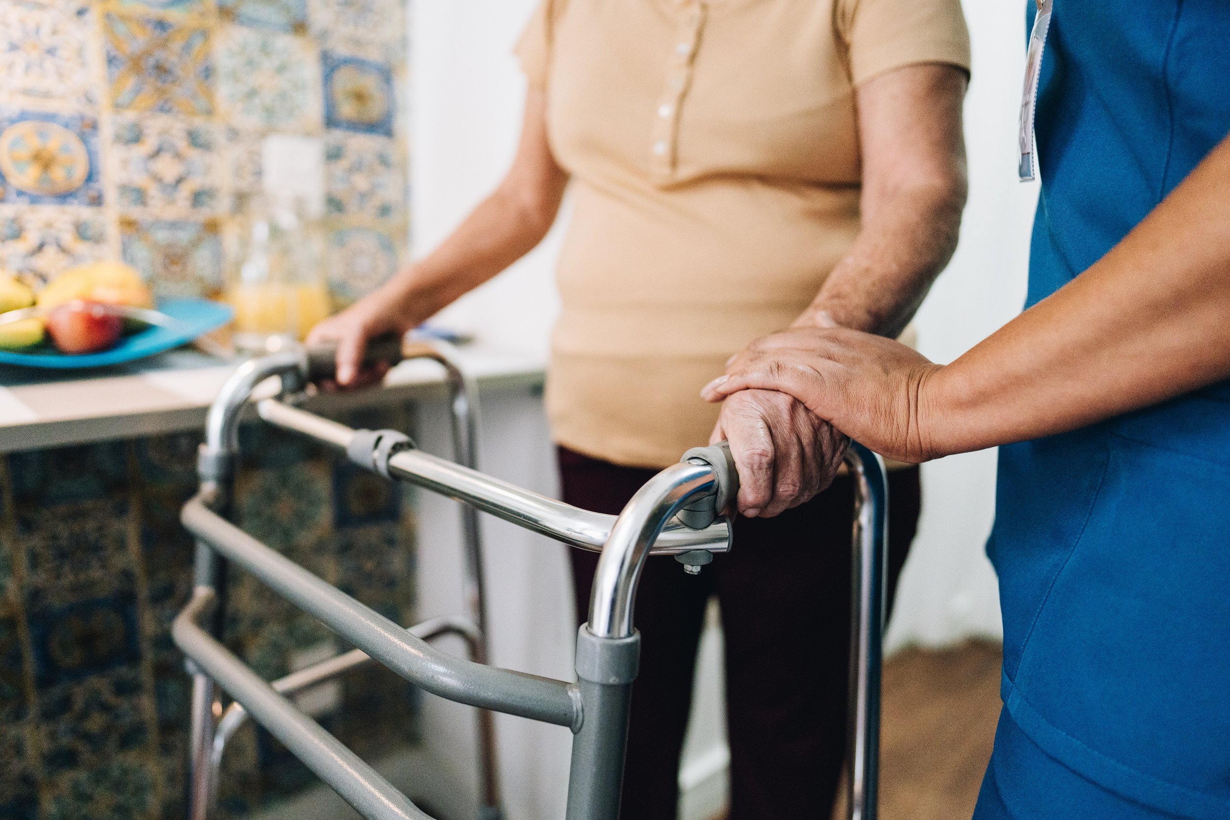 A healthcare worker helping an elderly person with a walker in a home or care facility setting.