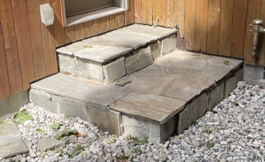 A set of stone steps made with large rectangular concrete blocks, leading up to a wooden wall with a small ledge. Before.