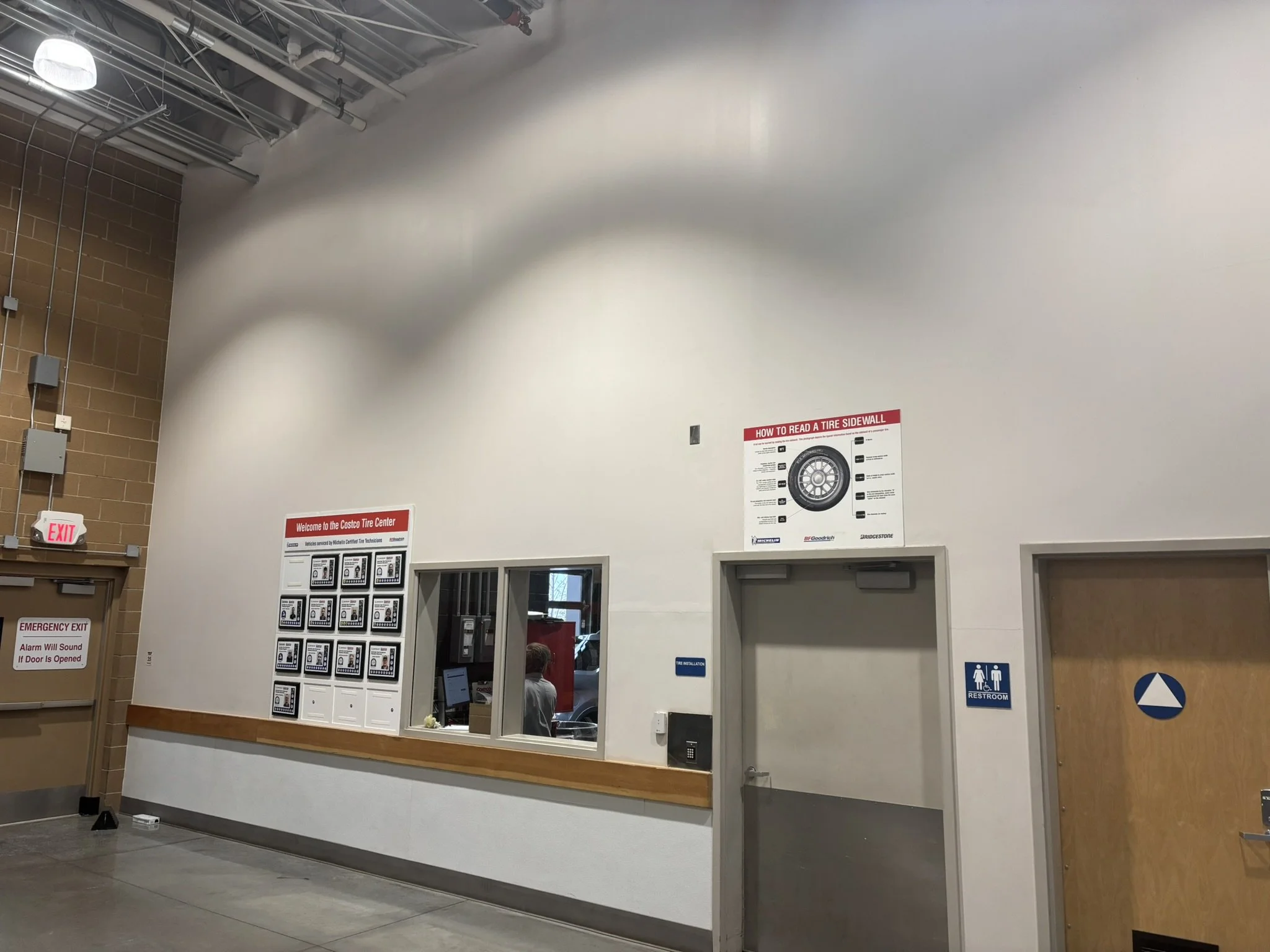 Before picture of the awards wall at the entrance to the Traverse City Costco tire center showing white walls, gray door. 