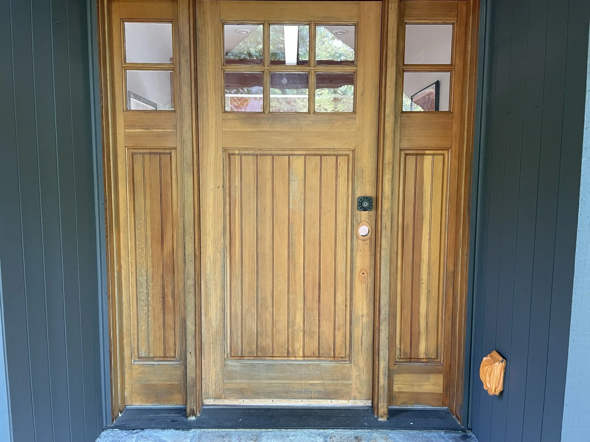 A wooden front door with glass panes at the top, framed by matching wood panels with glass insets on either side. Before.