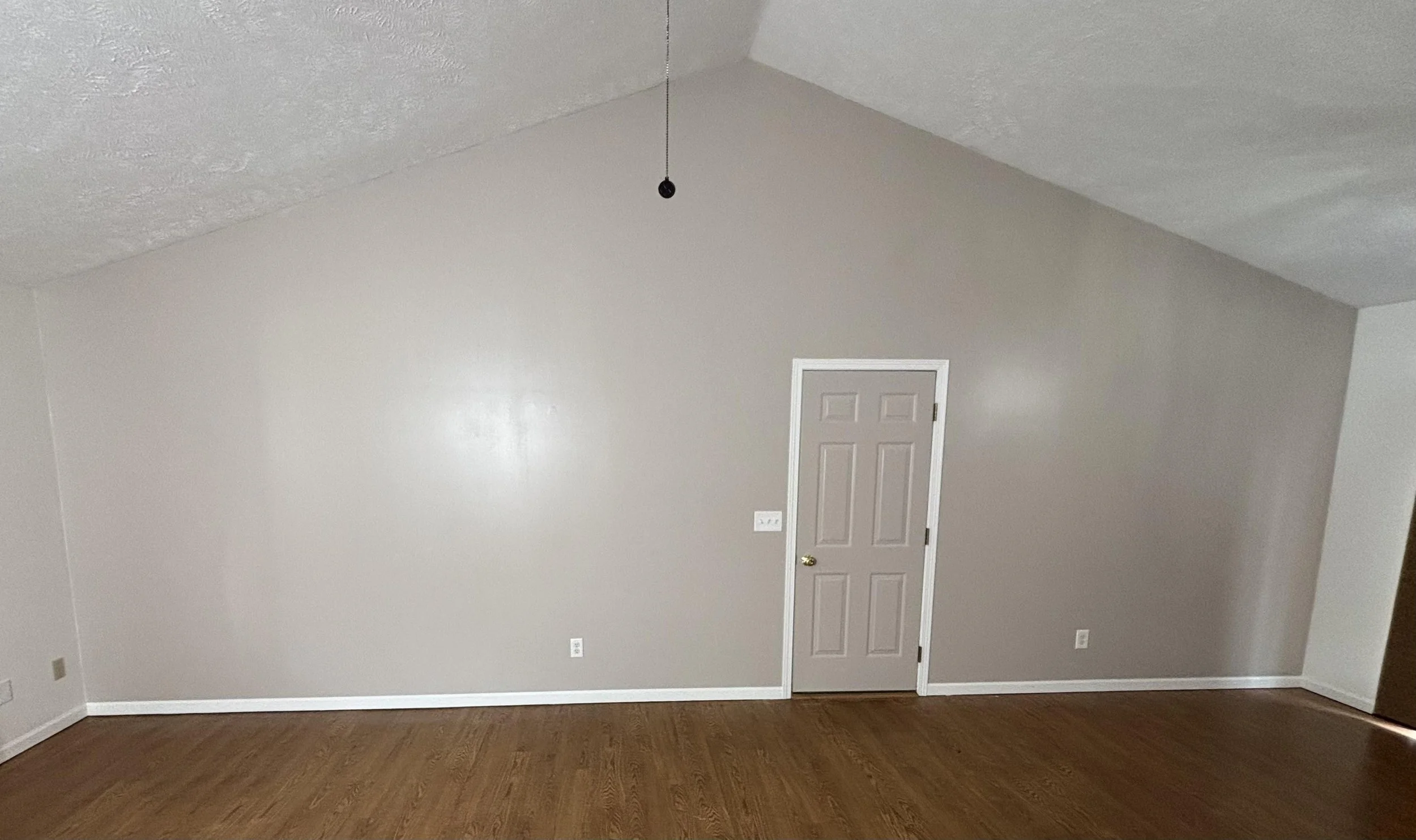 After picture of a living room with beige walls, wooden floor, white trim and beige door,