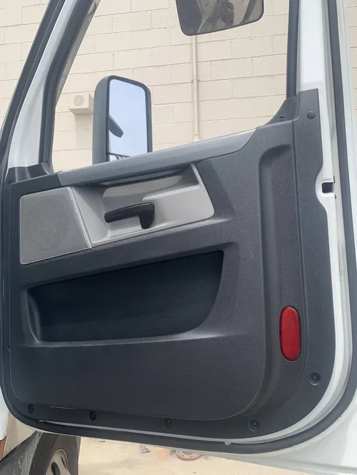 Close-up of the interior side of a vehicle door, showing a door handle, a small storage compartment, a speaker, and a red reflector light.