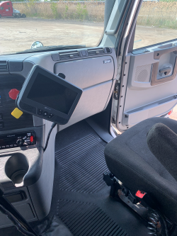 Interior of a vehicle with a dashboard, steering wheel, and passenger seat, featuring a mounted electronic device or monitor on the dashboard.