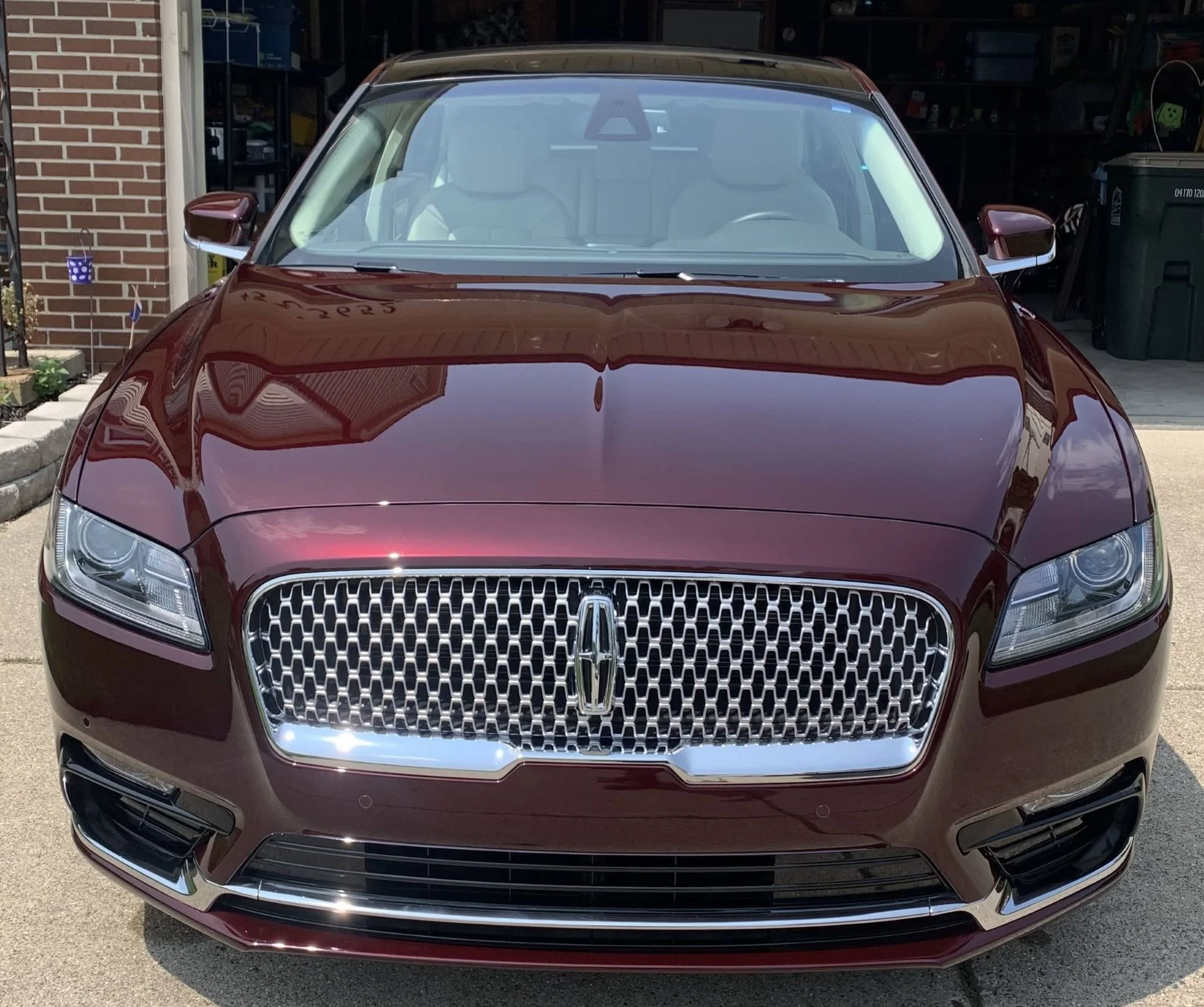 Front view of a maroon luxury sedan with a distinctive front grille, parked in a driveway in front of a garage.