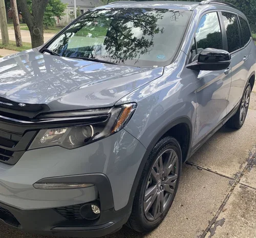 Gray SUV parked on a street with trees and houses in the background.