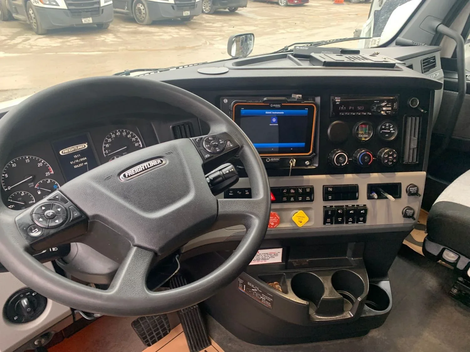The interior of a commercial truck or lorry cockpit, showing a steering wheel, dashboard with gauges, controls, and a digital screen.