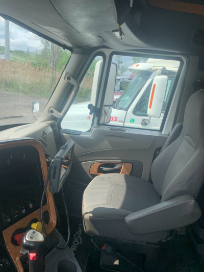 The interior of a semi-truck cab with a large windshield showing another semi-truck parked outside.