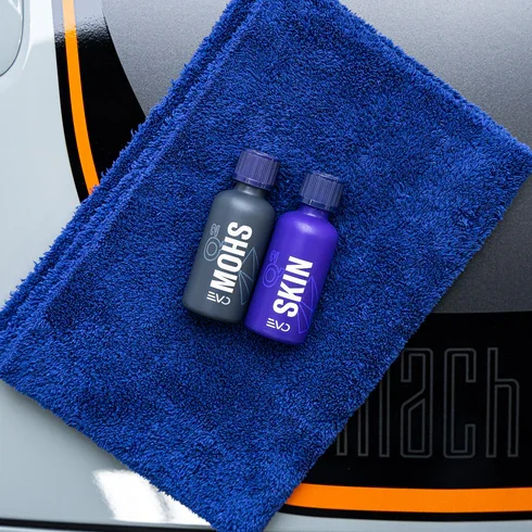Two small bottles of grooming products placed on a folded blue towel, on a larger gray towel with orange and black detailing.