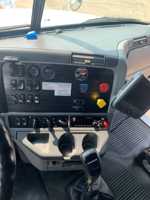 View of the truck dashboard showing various control switches, dials, a GPS device, and cup holders.