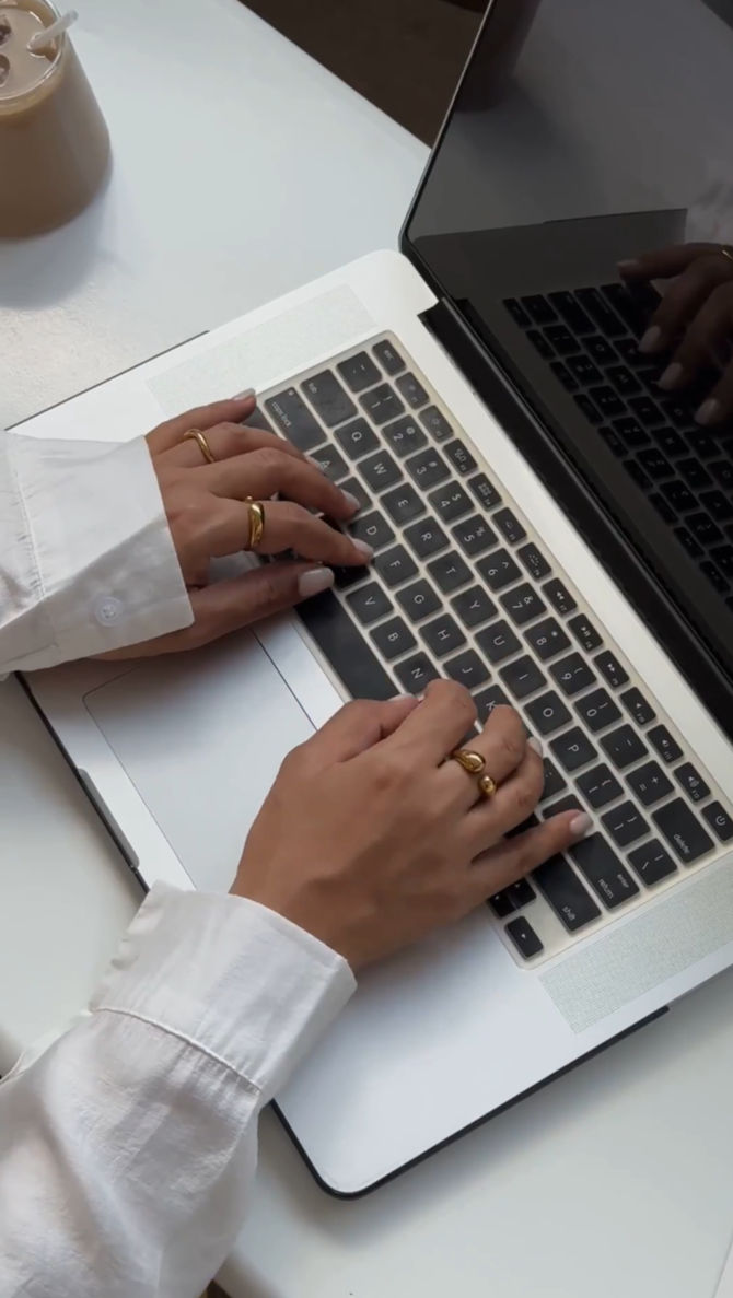 Person typing on a laptop keyboard with a cup of iced coffee nearby.