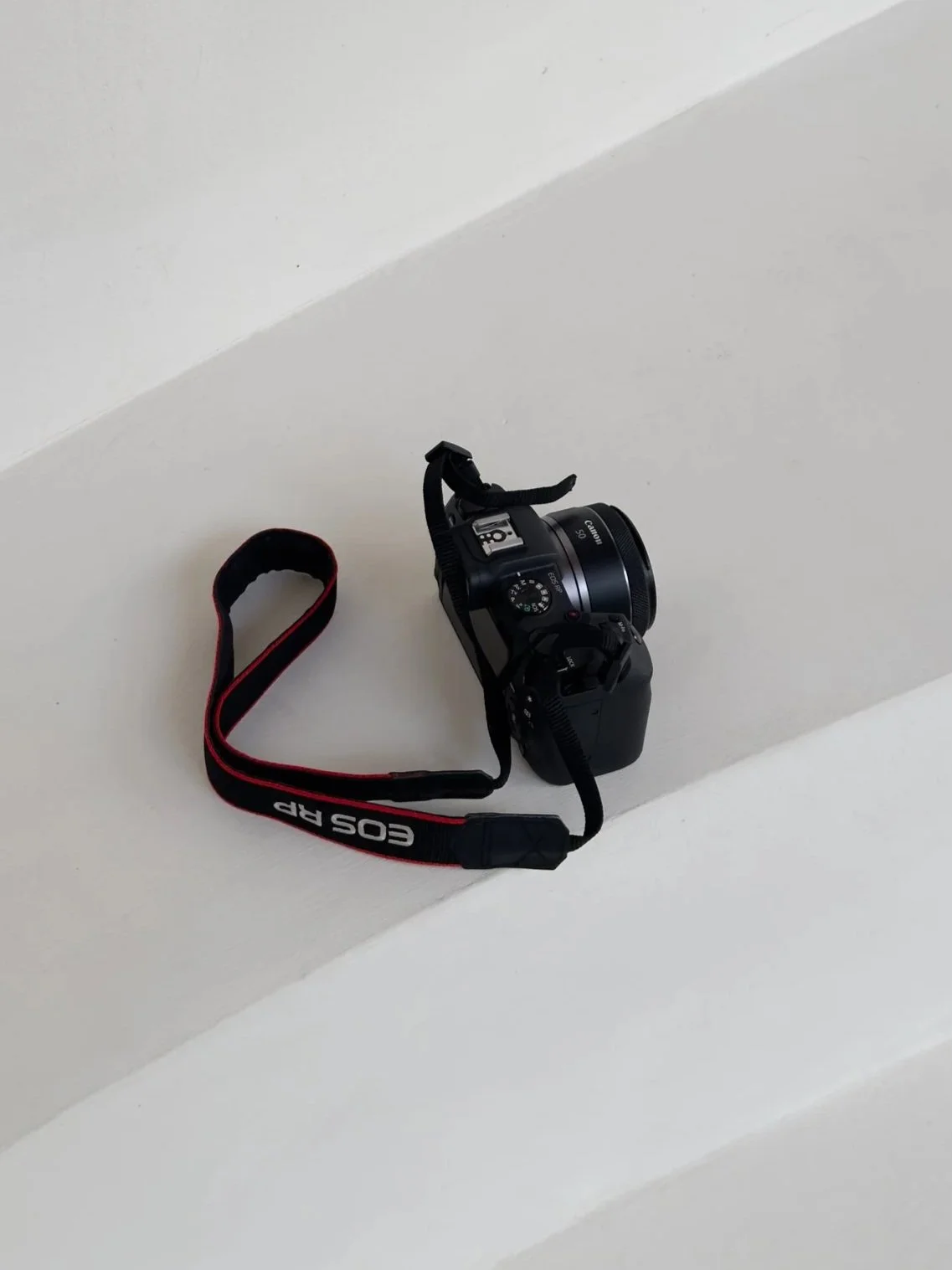A black Canon EOS Rebel T6 camera with a red and black strap resting on a white ledge.