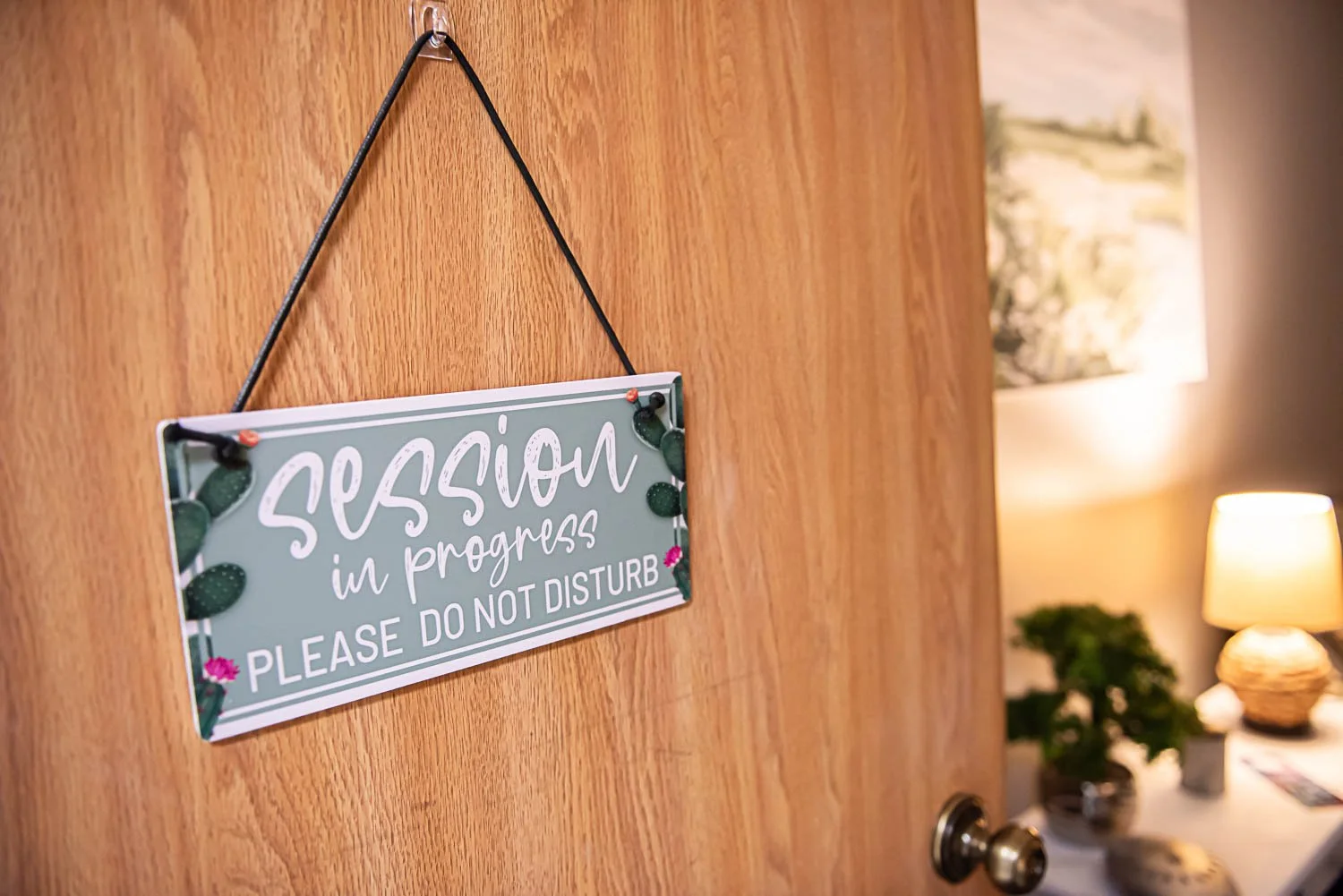 A door with a sign that says 'session in progress, please do not disturb' hanging on it, with a private counseling office at Anchored by Light Counseling, PLLC, visible in the background.