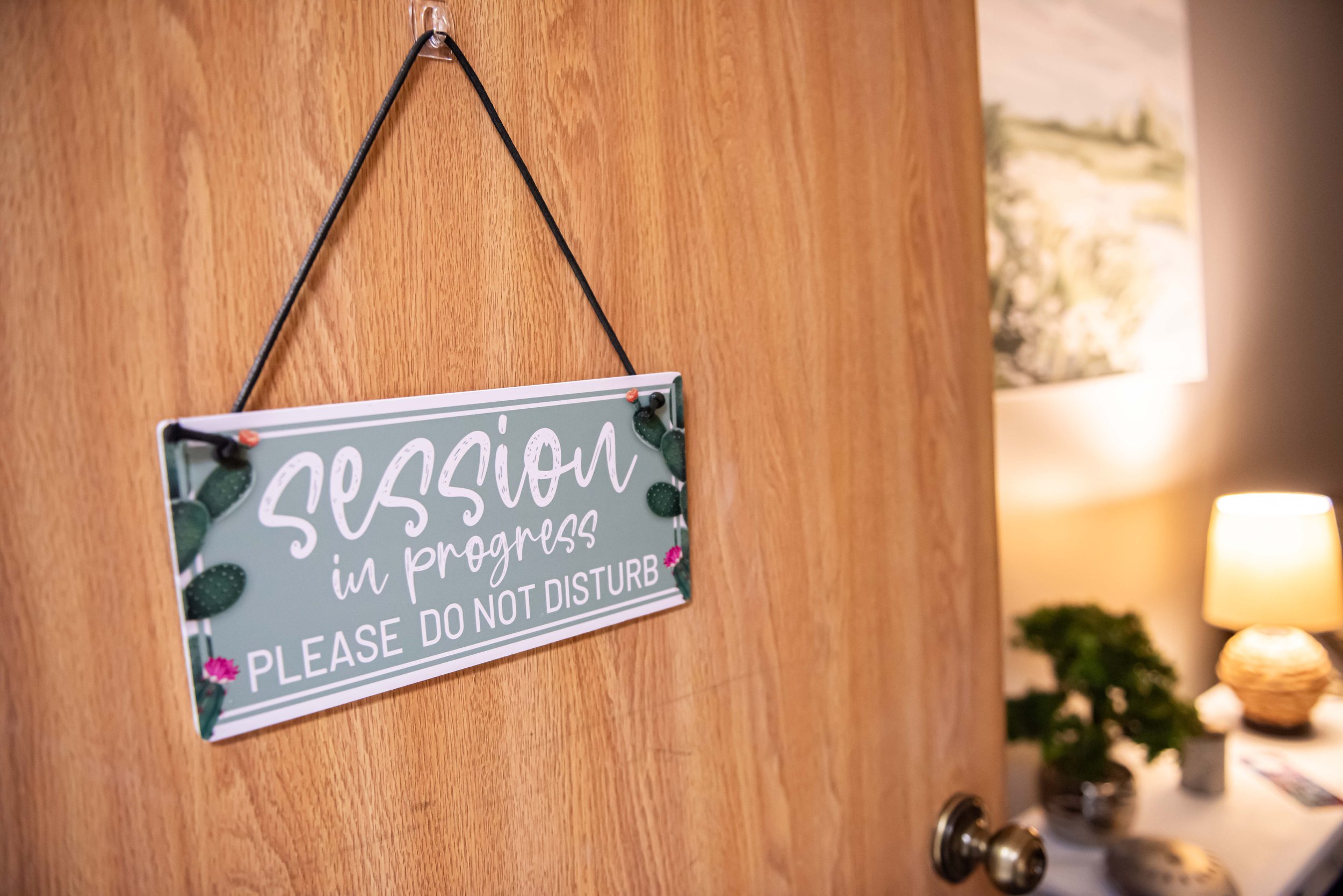 A door with a sign that says 'session in progress, please do not disturb' hanging on it, with a private counseling office at Anchored by Light Counseling, PLLC, visible in the background.