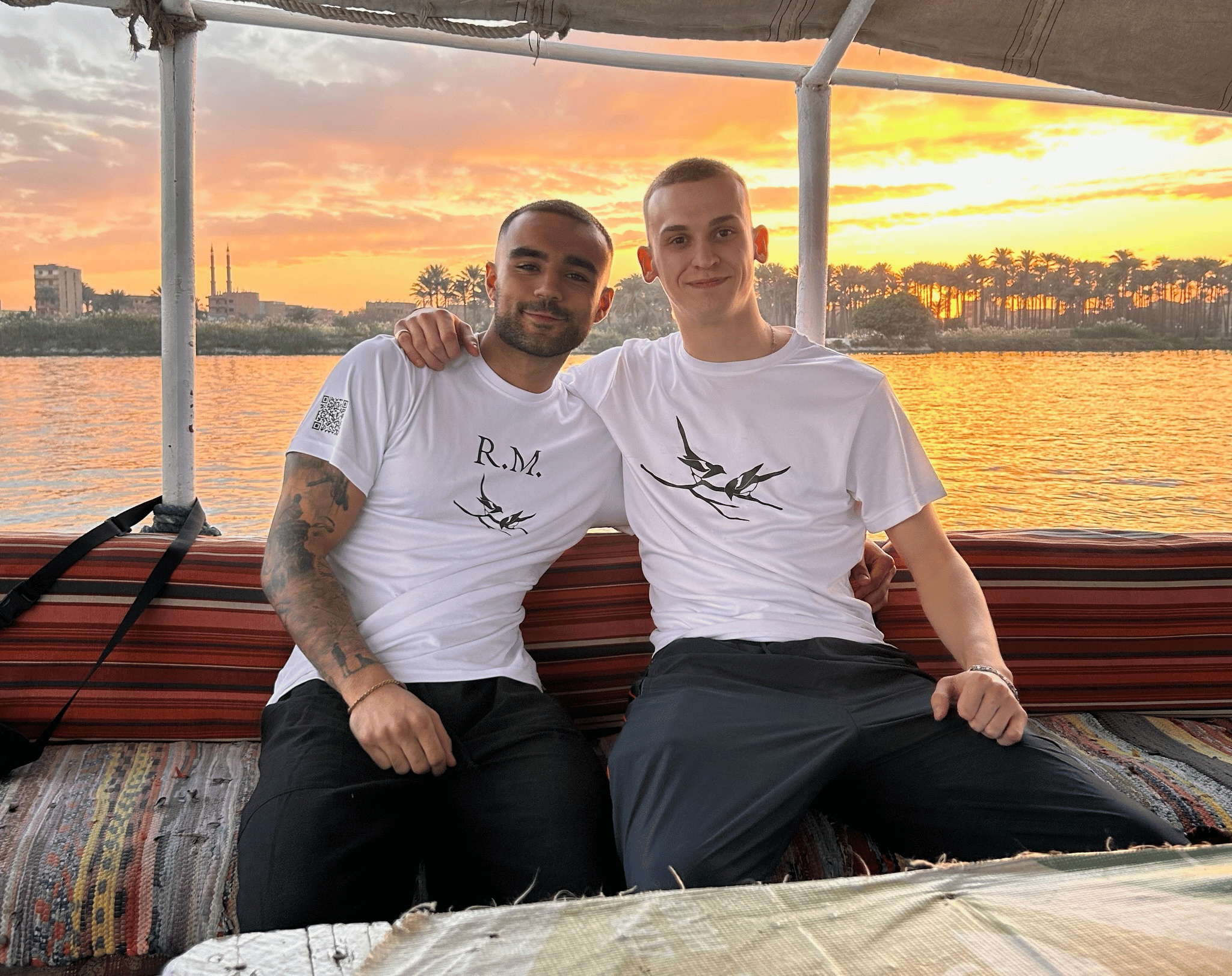 Rohan and Tom wearing Mission Planet T-shirts while travelling by boat during a sunset mission journey