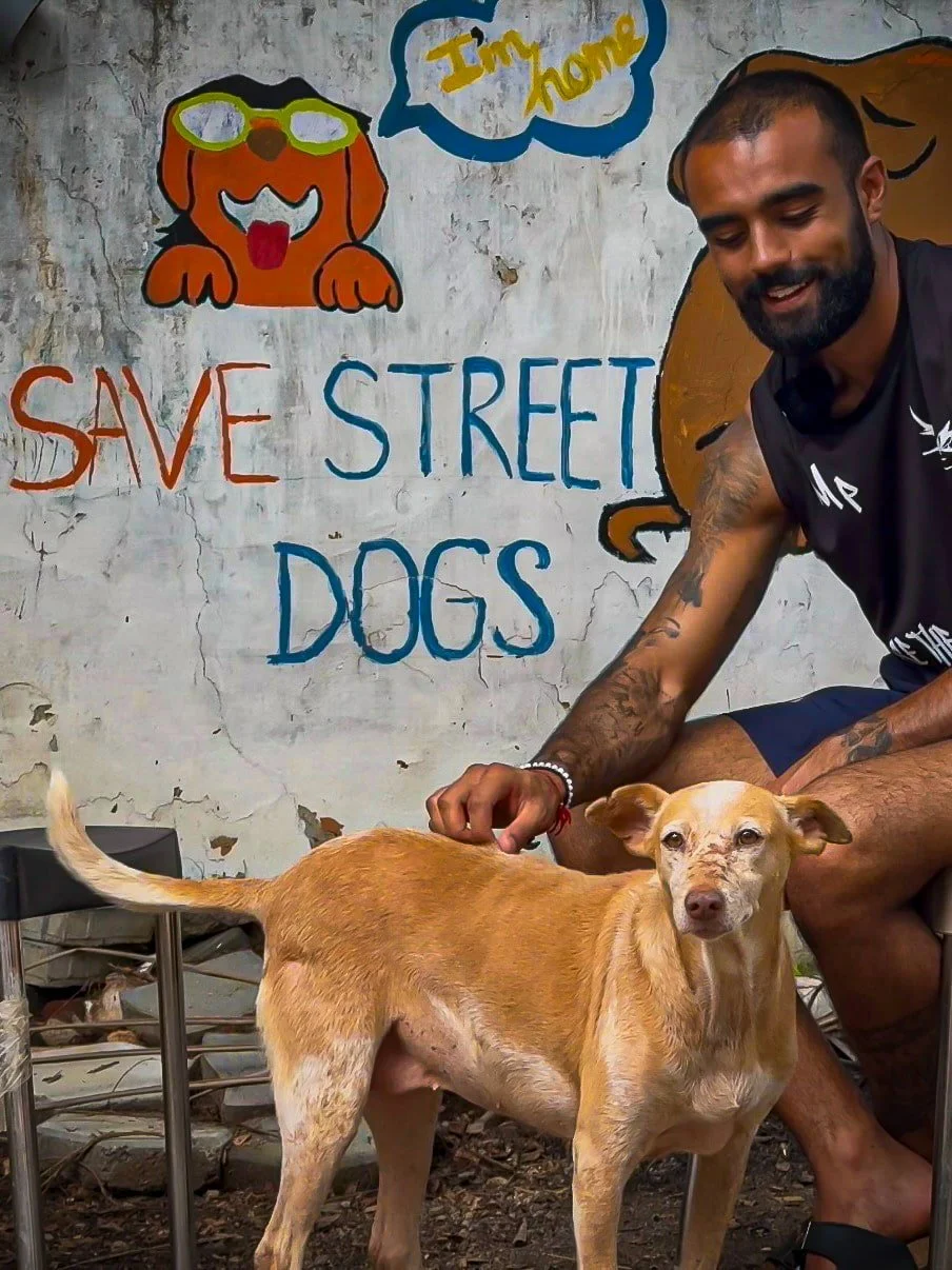 Rohan from The Mission Planet CIC with a rescue dog in front of a “Save Street Dogs” mural during an animal welfare initiative.