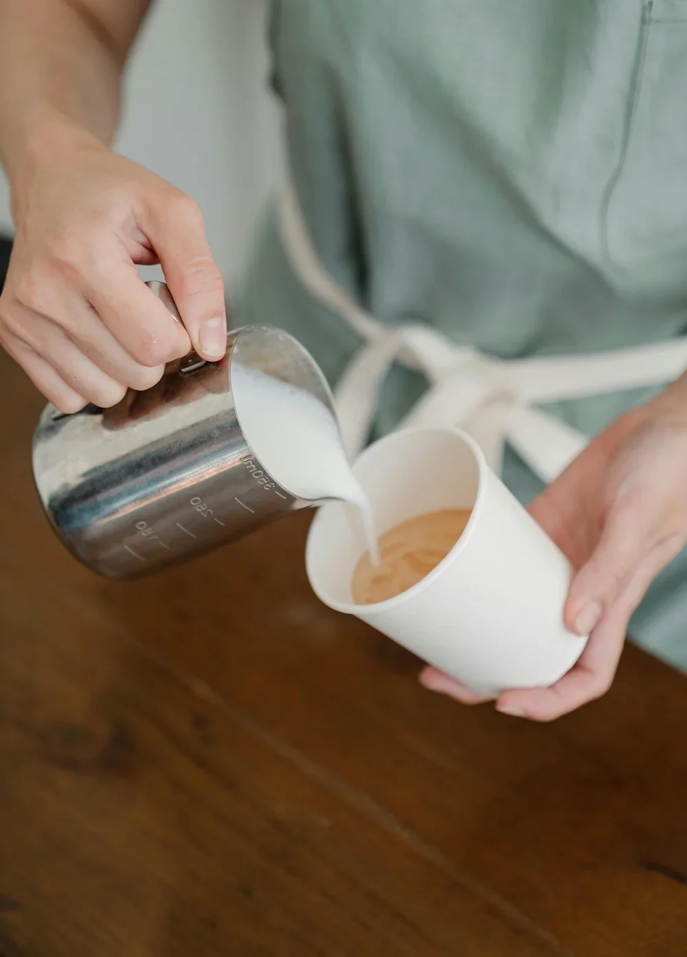 Person pouring milk into a paper cup with coffee