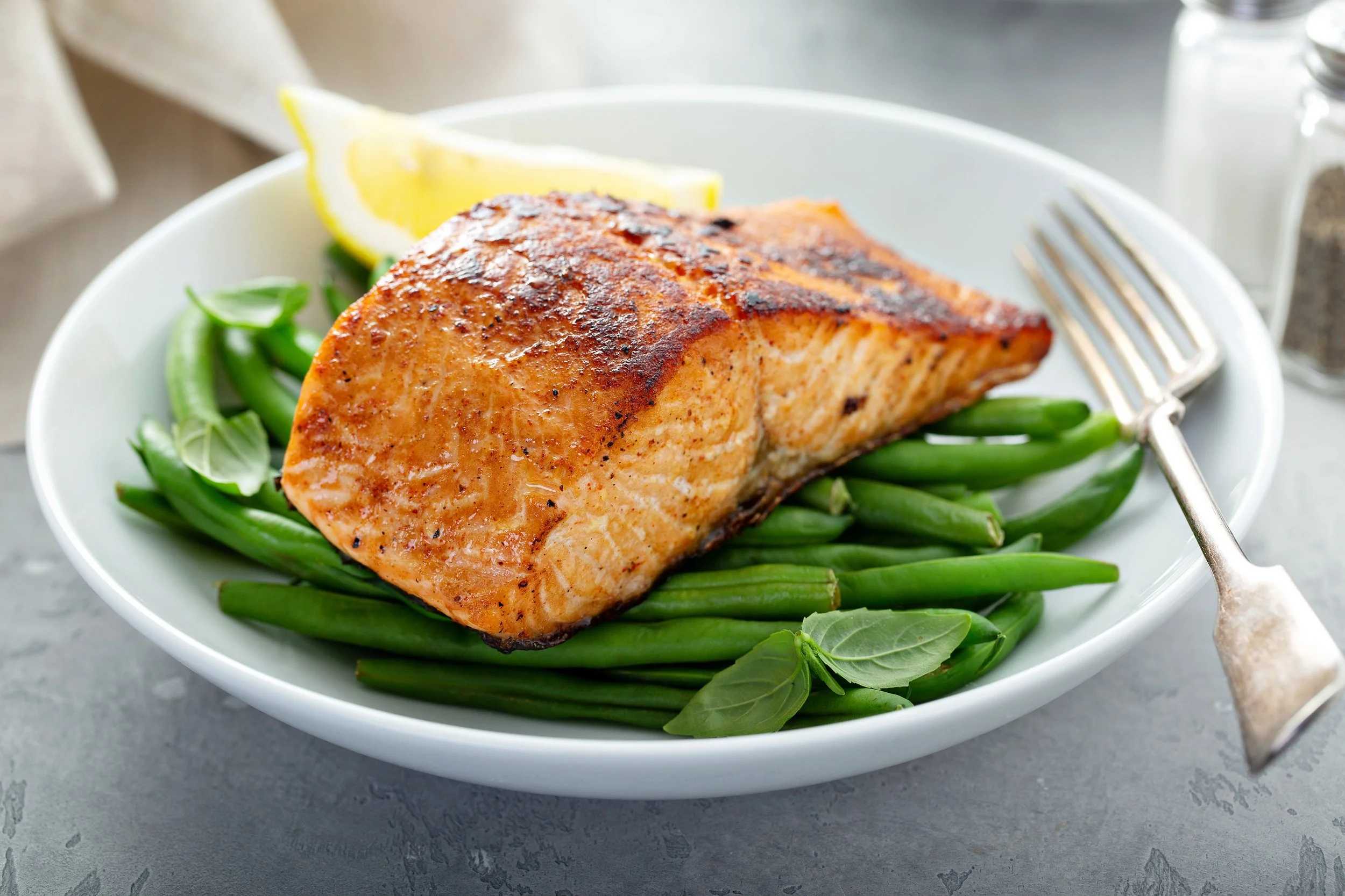 Grilled wild salmon served with organic green beans and lemon wedge on a white plate