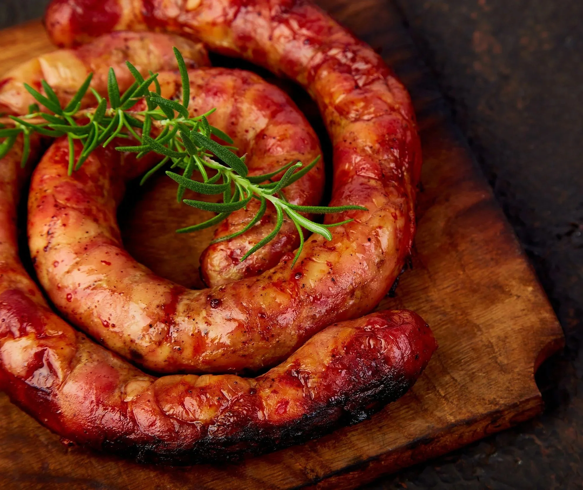 Grilled homemade pork sausage ring with rosemary on butcher block