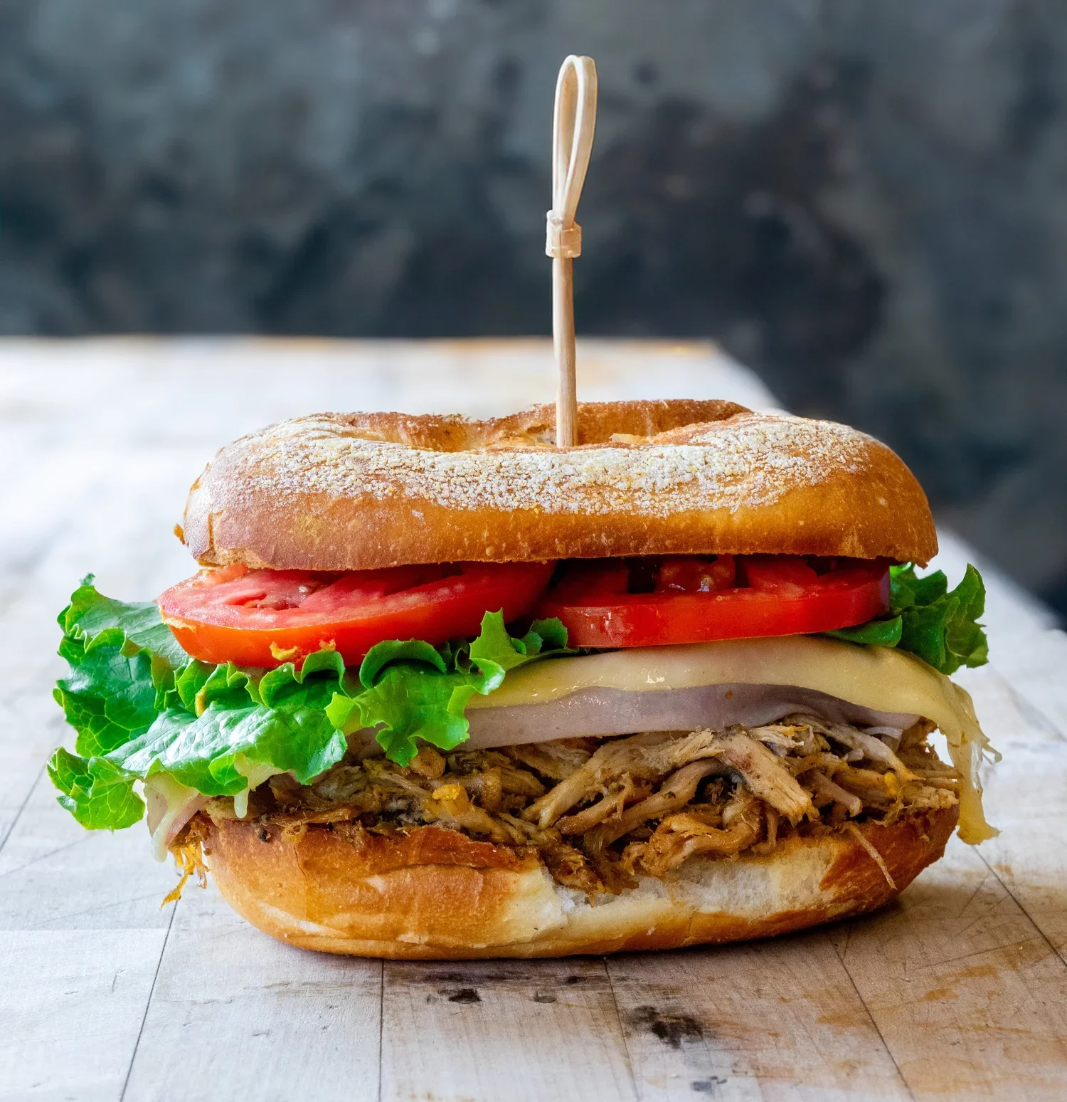 A large sandwich with shredded meat, lettuce, tomato slices, cheese, and a bun