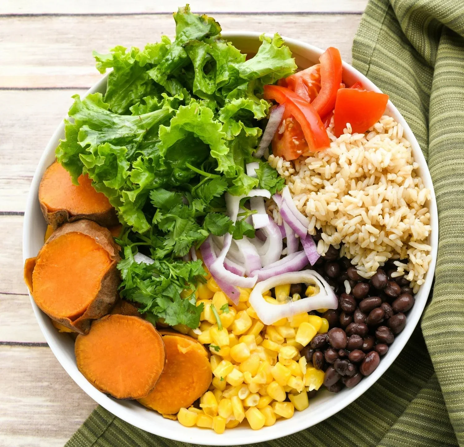 Bowl of salad with lettuce, sweet potatoes, cilantro, red onion, rice, tomatoes, black beans, corn
