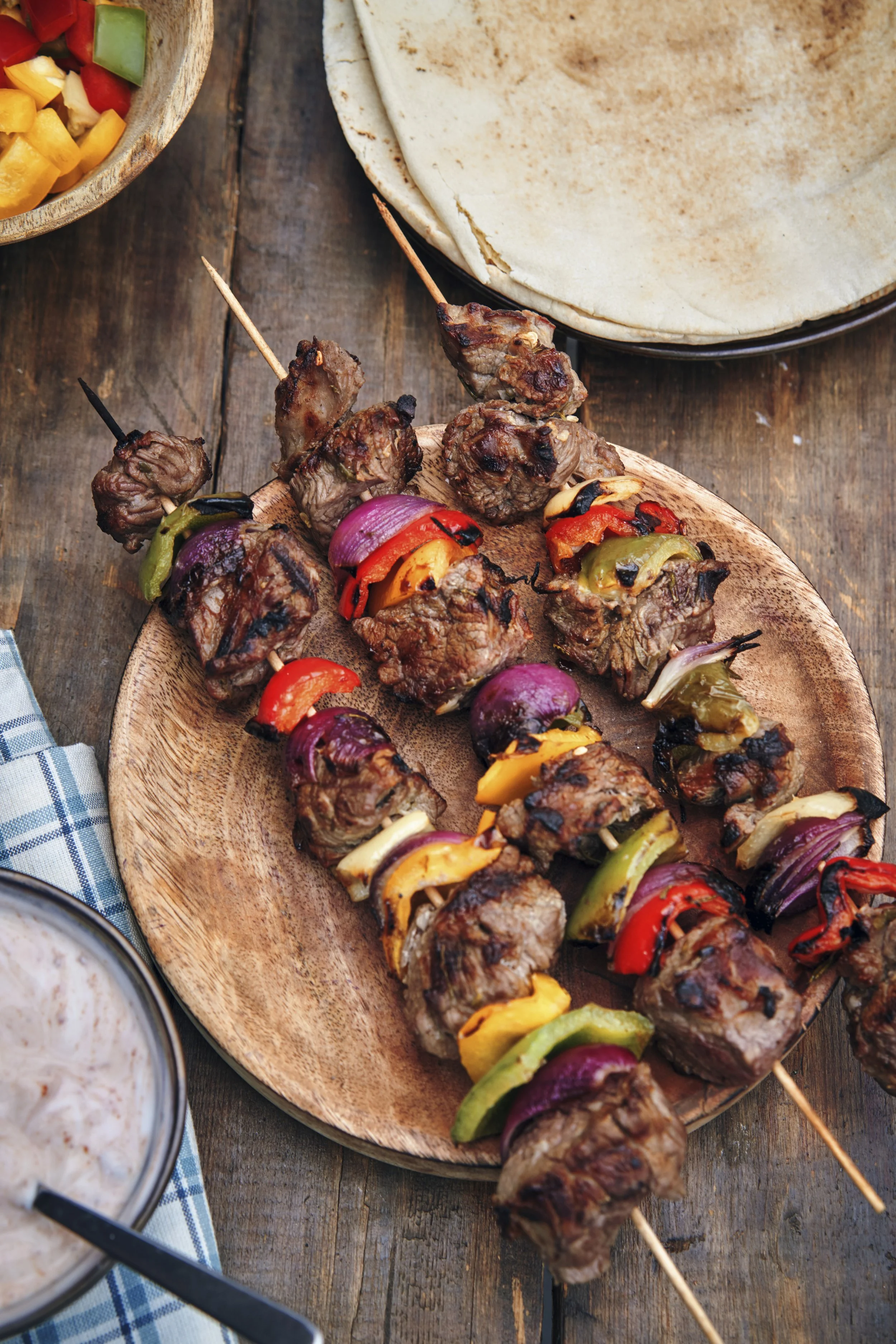 Grilled lamb kebabs with vegetables on wood skewers with flat bread on rustic picnic table