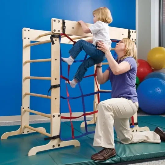 Child climbing on an indoor therapy climbing wall with help from a therapist.