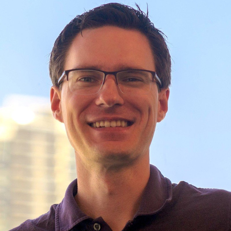 A photo of Dihedral Chief Product Officer Alban Vignaux, with dark hair, glasses, and a broad smile, standing outdoors with a blurred background of a building and a clear blue sky.