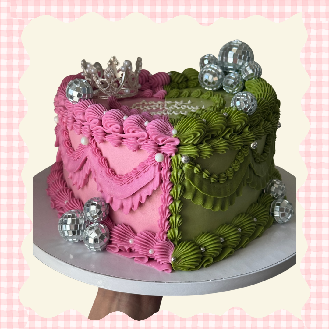 A colorful birthday cake decorated with pink and green frosting, silver disco ball ornaments, and a silver crown on top, set against a pink gingham background.