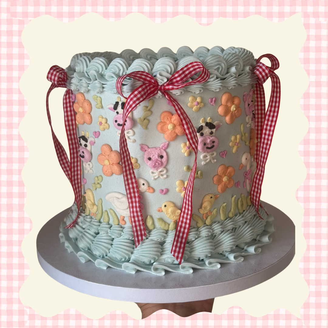 Decorated cake with pastel blue frosting, featuring farm animal and flower designs, red and white checkered ribbons, and piped ruffles around the top and bottom edges.