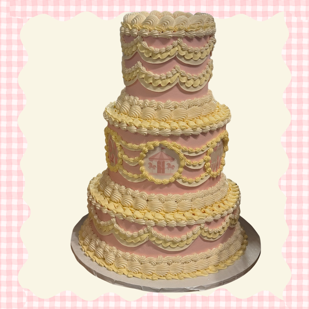 Tall, pink and white tiered cake with decorative icing swirls and a carousel horse design on the middle tier, set against a light background with pink gingham border.