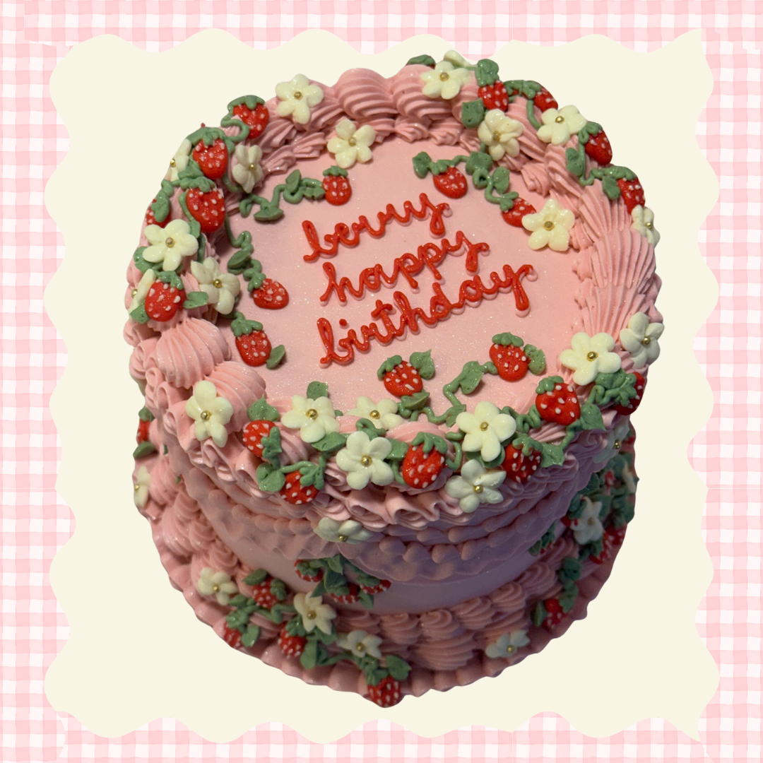 Pink birthday cake decorated with strawberries, white flowers, and green leaves, with the message "Lovely happy birthday" written on top.
