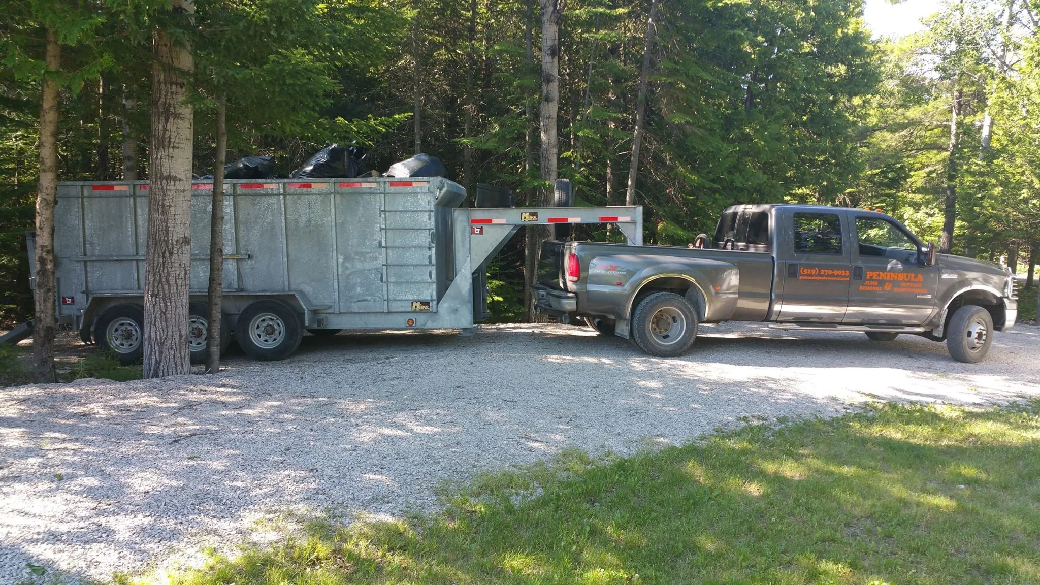 Peninsula Junk Removal truck and dump trailer loaded with junk bags parked on a gravel driveway in Bruce Peninsula
