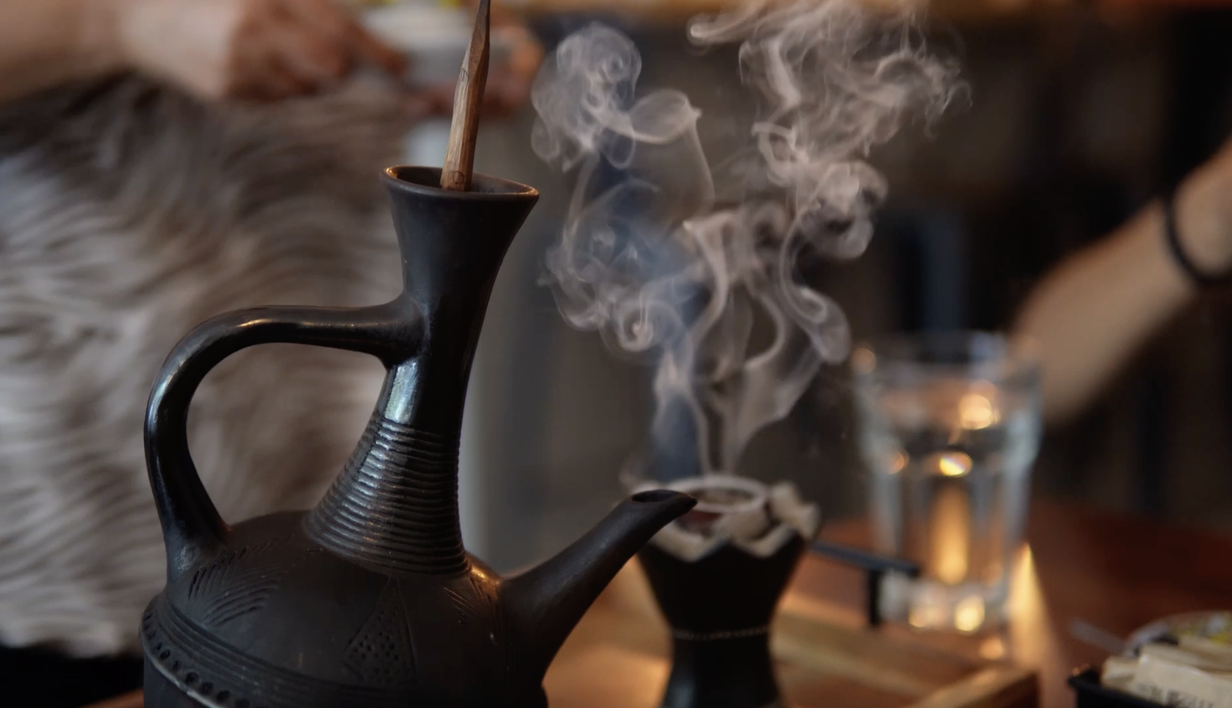 A black teapot with steam rising from its spout, placed on a wooden surface, in a cozy dining setting.
