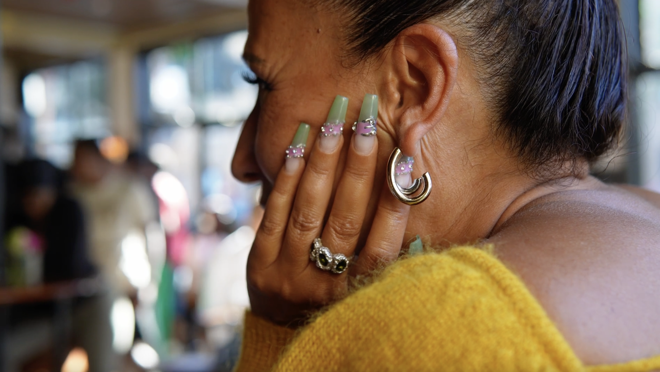 Close-up of a woman with dark hair wearing jewelry, touching her ear, in a store setting with blurred background.