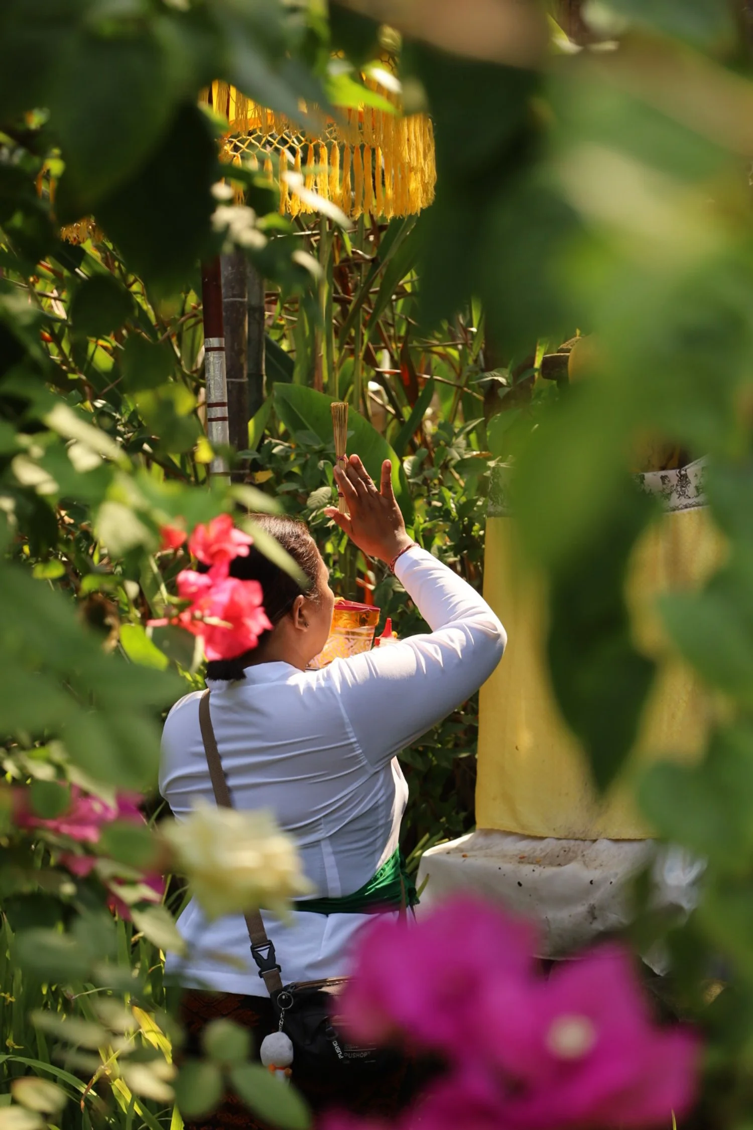 A woman in traditional attire performing a religious or cultural ceremony in a lush, green garden surrounded by colorful flowers and foliage.