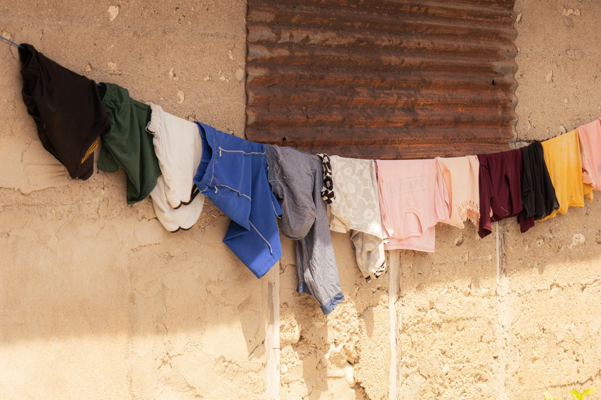 Clothes hanging on a clothesline against a wall with a rusty metal sheet.