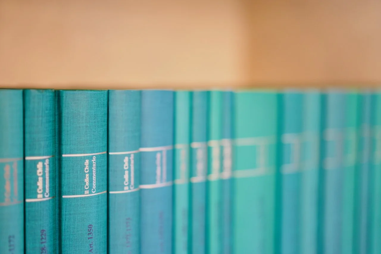 Lungo una mensola vi sono libri di colore turchese con scritte bianche e una riga viola, parzialmente visibili.