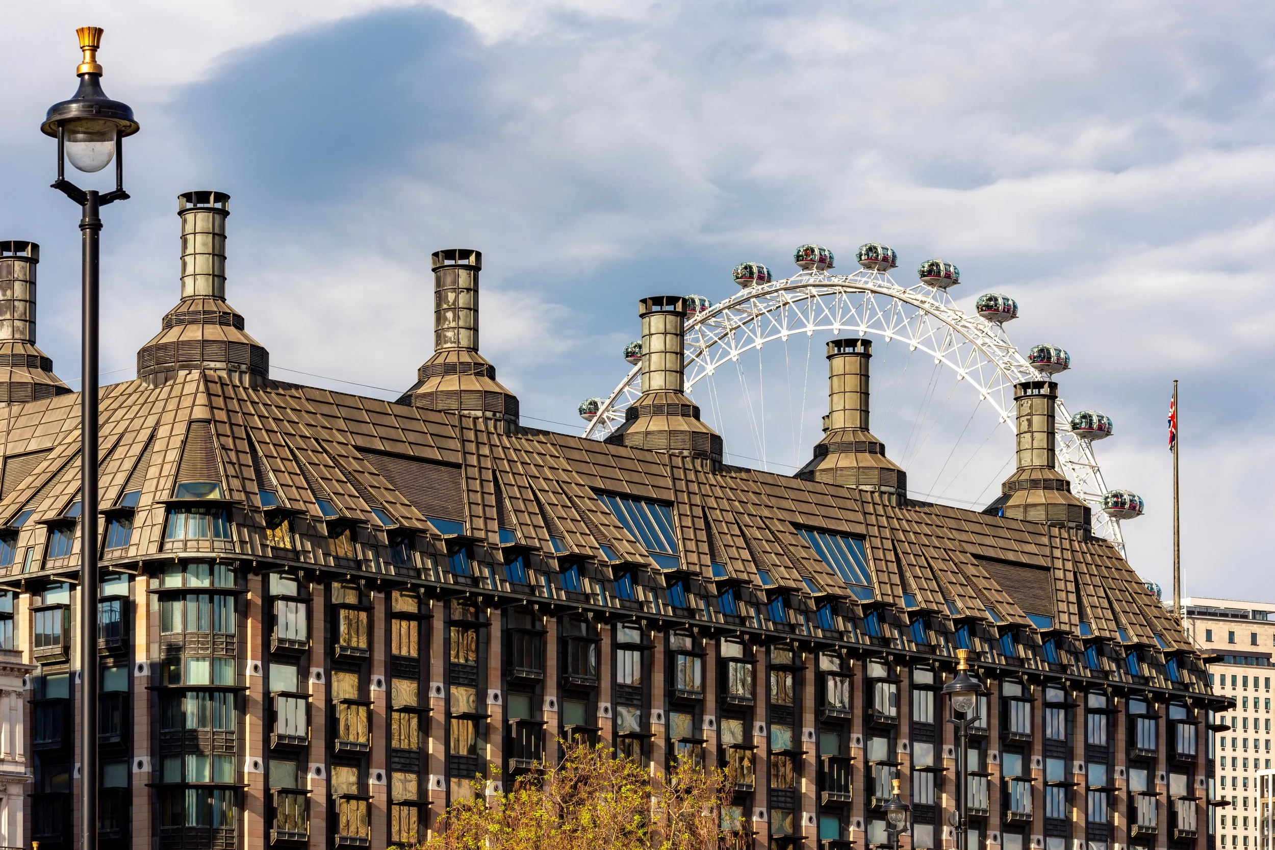 A building with a brown, tiled roof and multiple chimneys, with a large Ferris wheel in the background under a cloudy sky.
