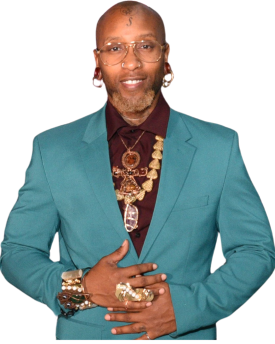 A man wearing glasses, a red plaid suit jacket, and a matching vest with a pocket square. He has a gold necklace with elephant charms, large gold earrings, and a patterned bow tie.