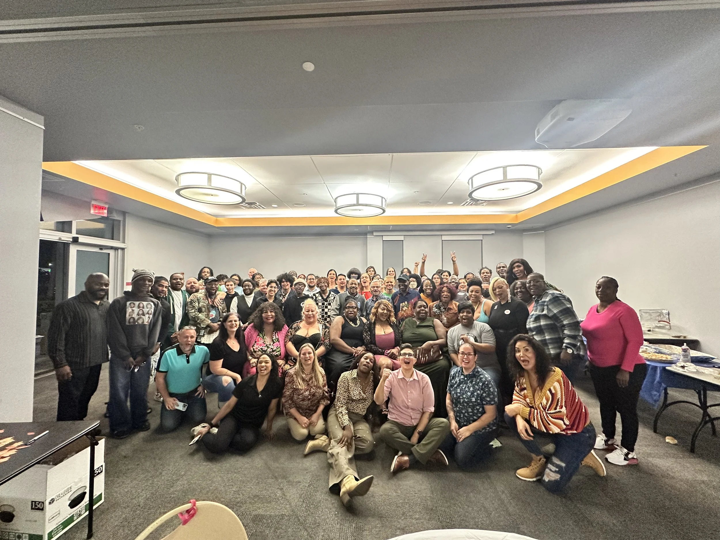 Group photo of smiling diverse people gathering in a banquet hall, some seated and some standing, celebrating an event.