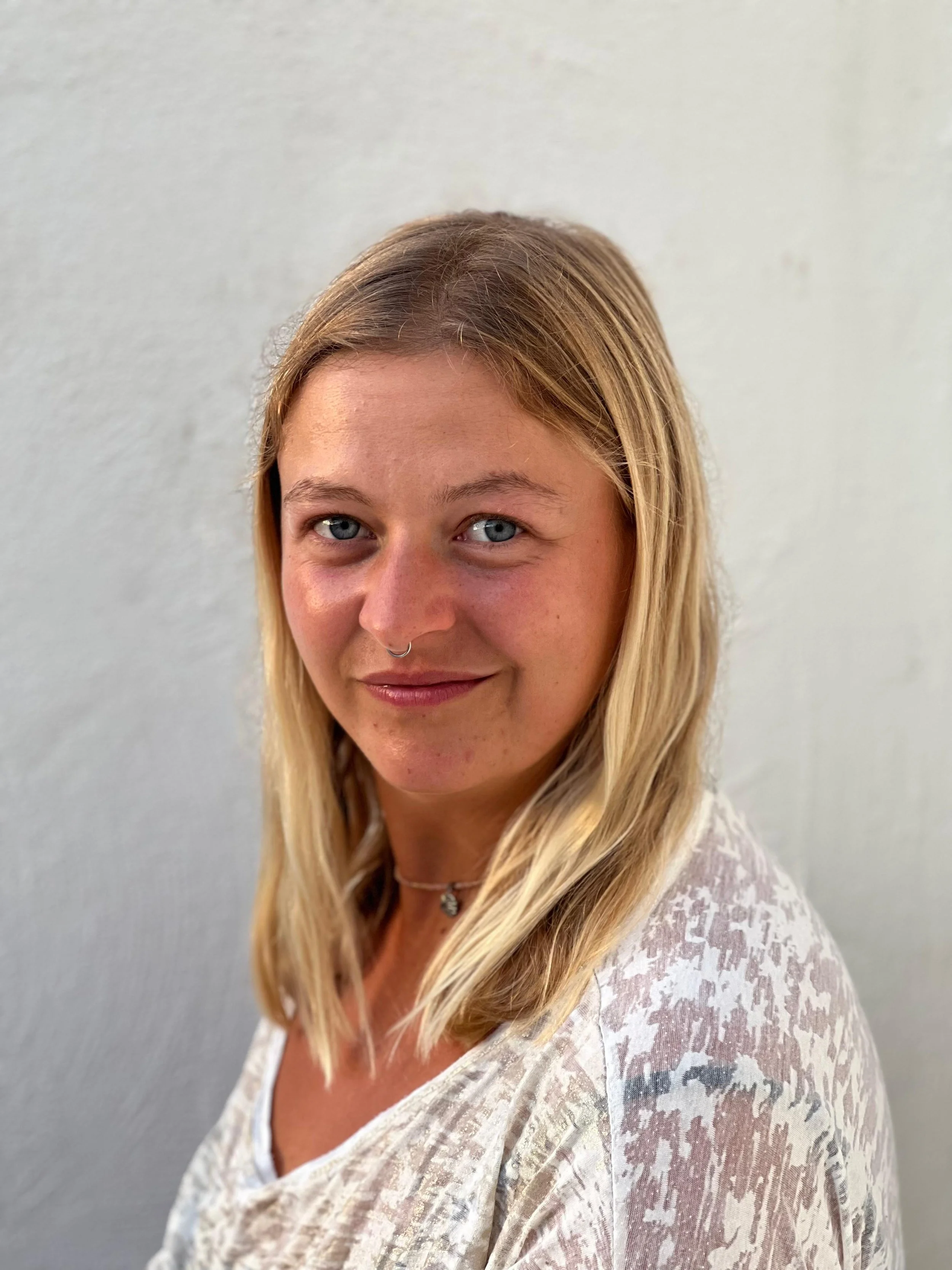 Foto von Svenja Schirdewahn. Eine junge Frau mit blonden, schulterlangen Haaren, die ein weißes T-Shirt trägt.